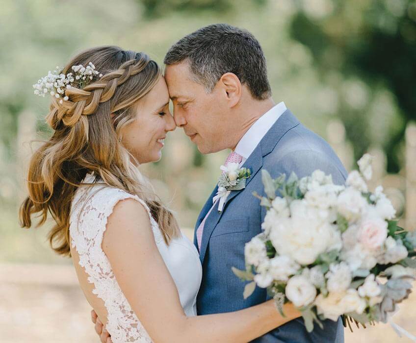 Smiling newlyweds embracing beside soft greenery