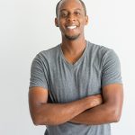 Smiling man in gray shirt, arms crossed.