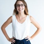 Smiling woman with glasses and hands on hips.