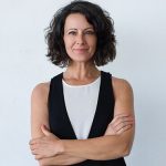 Woman with short hair, arms crossed, smiling.
