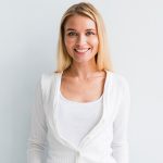 Smiling woman in white against light background.