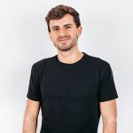 Man in black shirt smiling confidently.