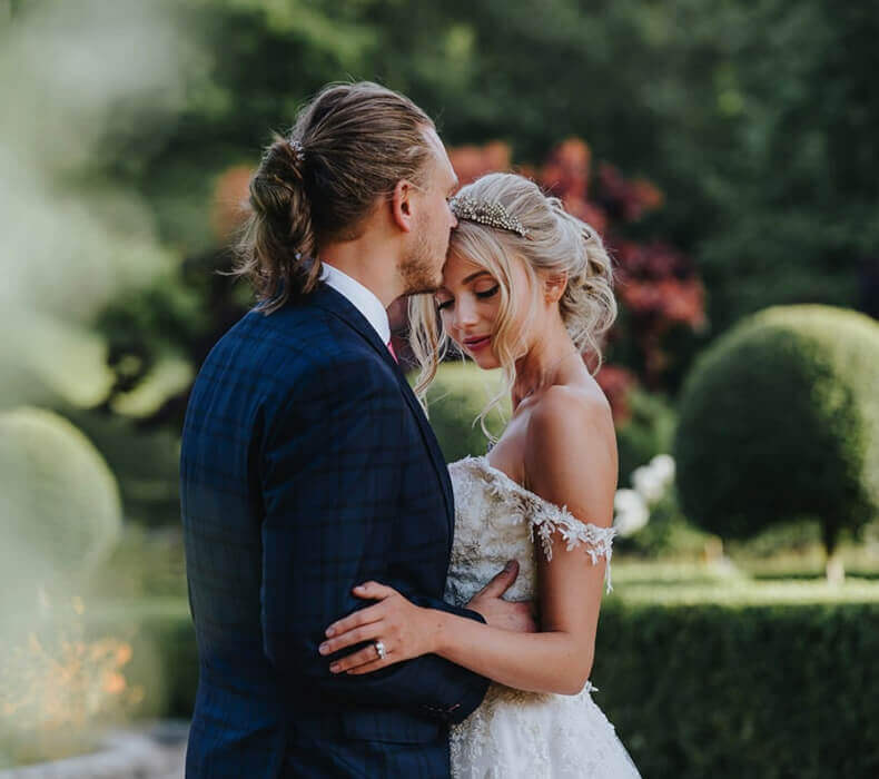 Bride and groom embracing in garden setting.